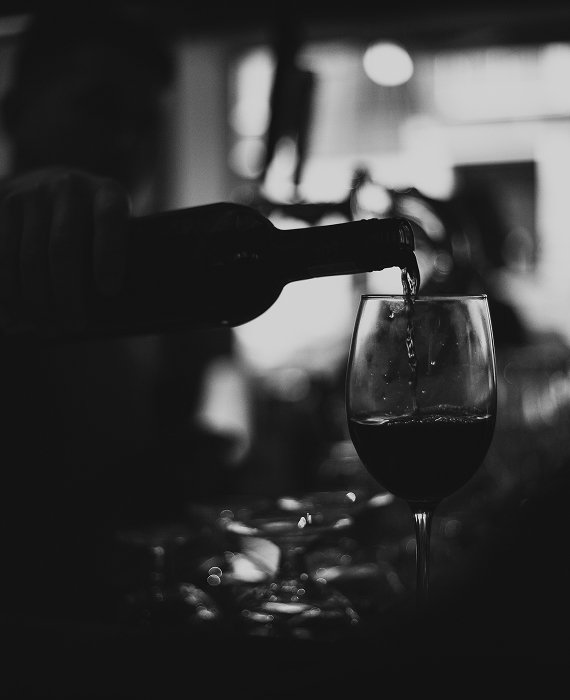 Vin rouge versé dans un verre à pied dans une ambiance tamisée, en arrière-plan flou