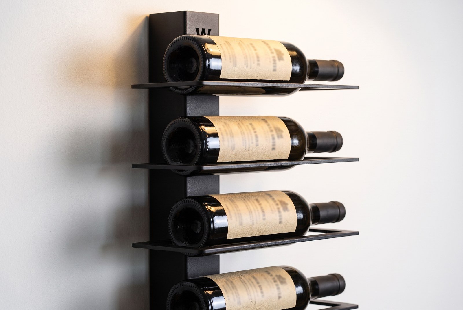 Gros plan sur des étiquettes de vin alignées en façade d'un mur de bouteilles, en lumière rasante