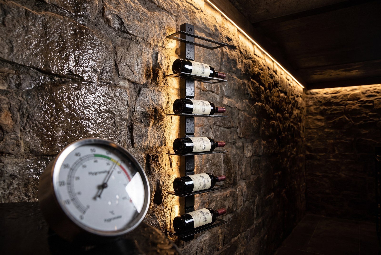 Hygromètre dans une cave humide devant une étagère à vin murale en acier laqué noir