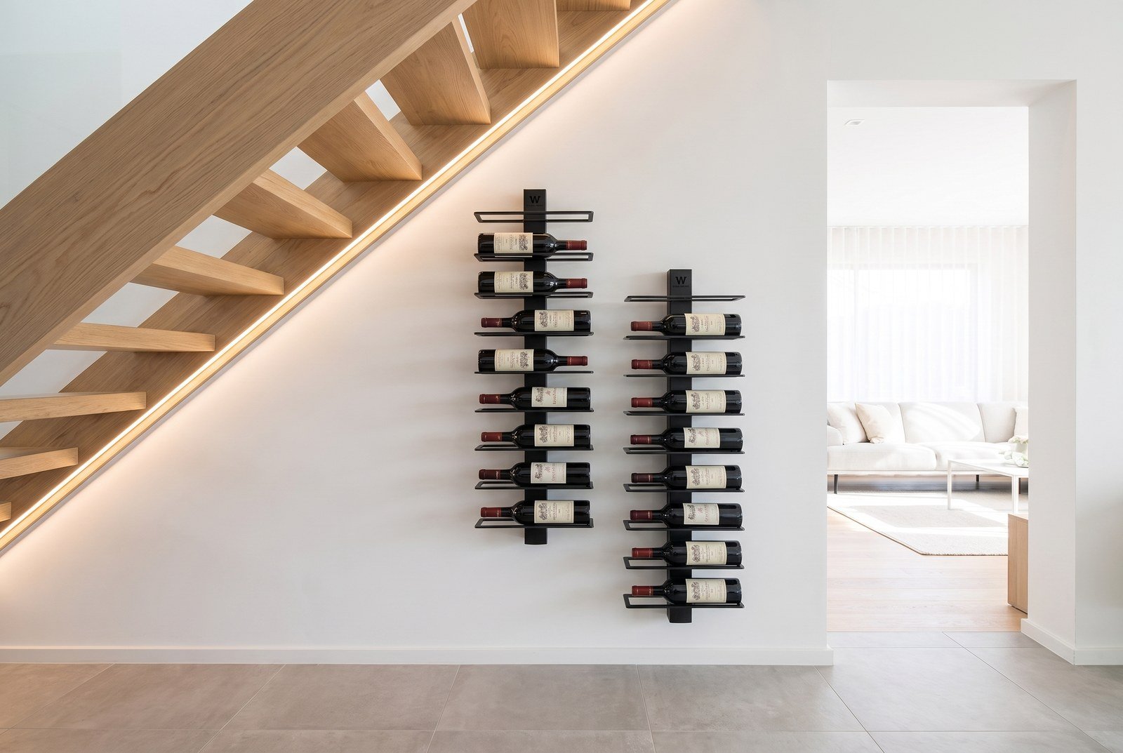 Mur à vin aménagé sous un escalier avec colonnes en acier noir et éclairage LED intégré