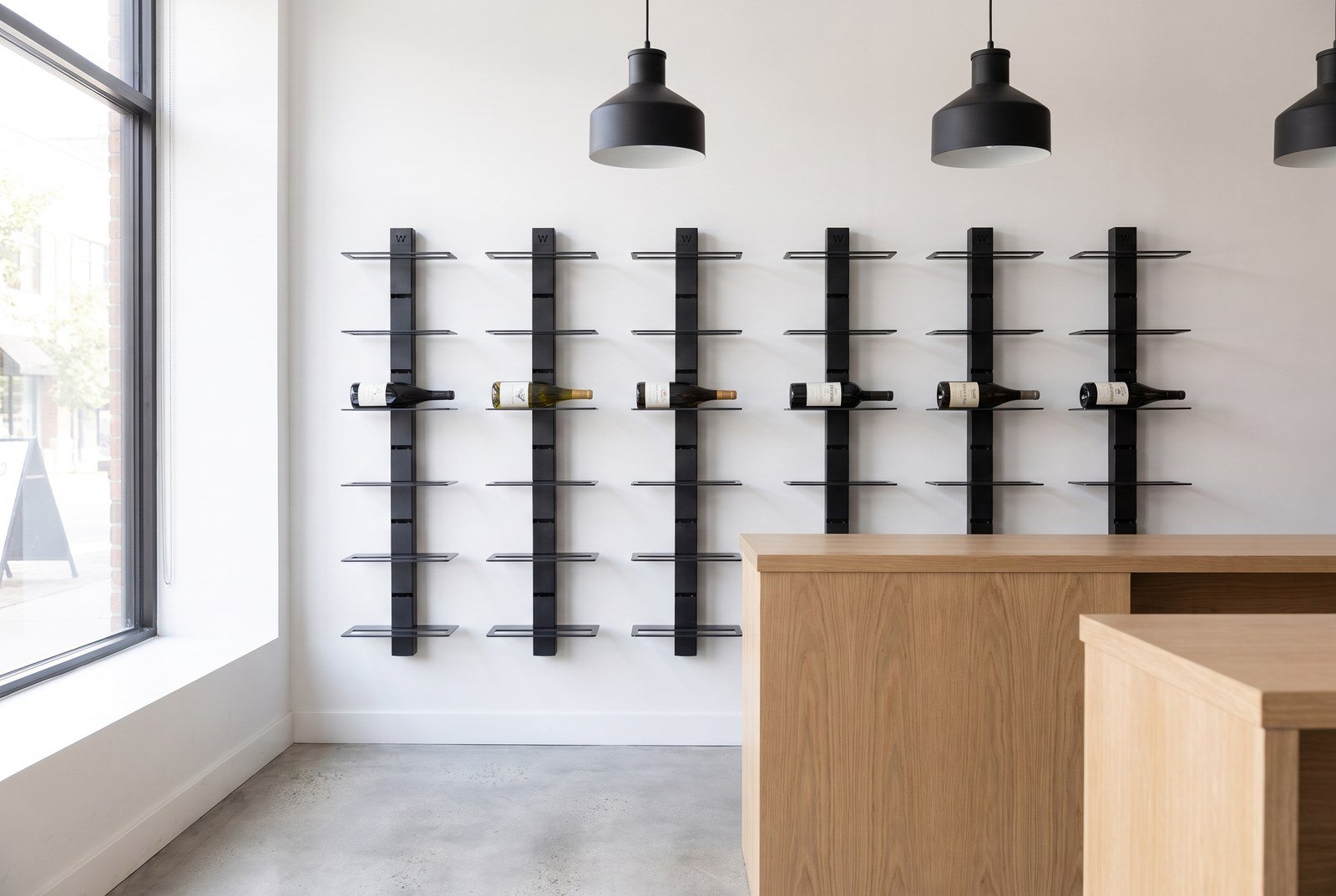 Mur de bouteilles derrière le comptoir d'un caviste, sélection du moment placée à hauteur d'œil