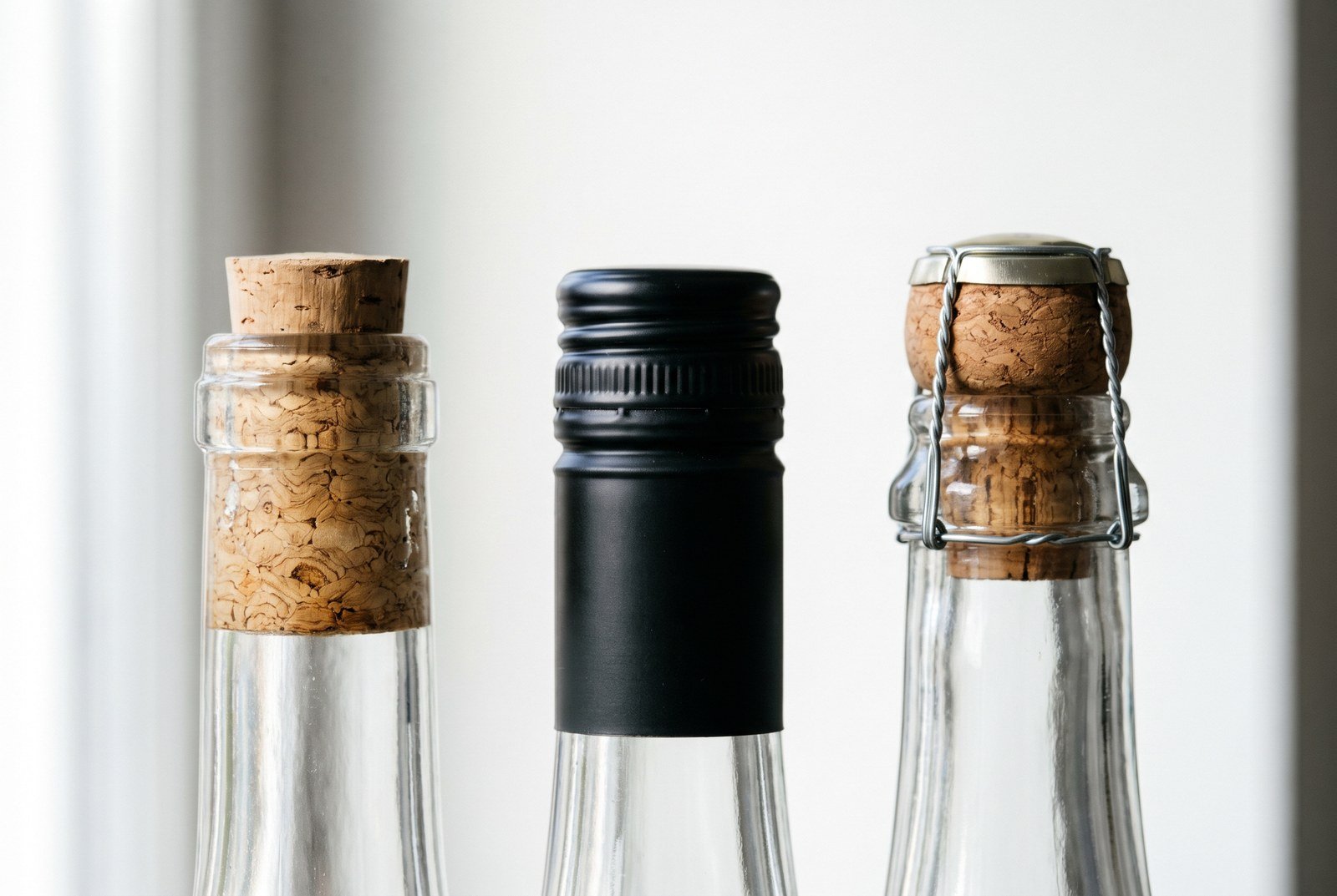 Gros plan sur trois fermetures de bouteille : bouchon de liège, capsule à vis et muselet de champagne